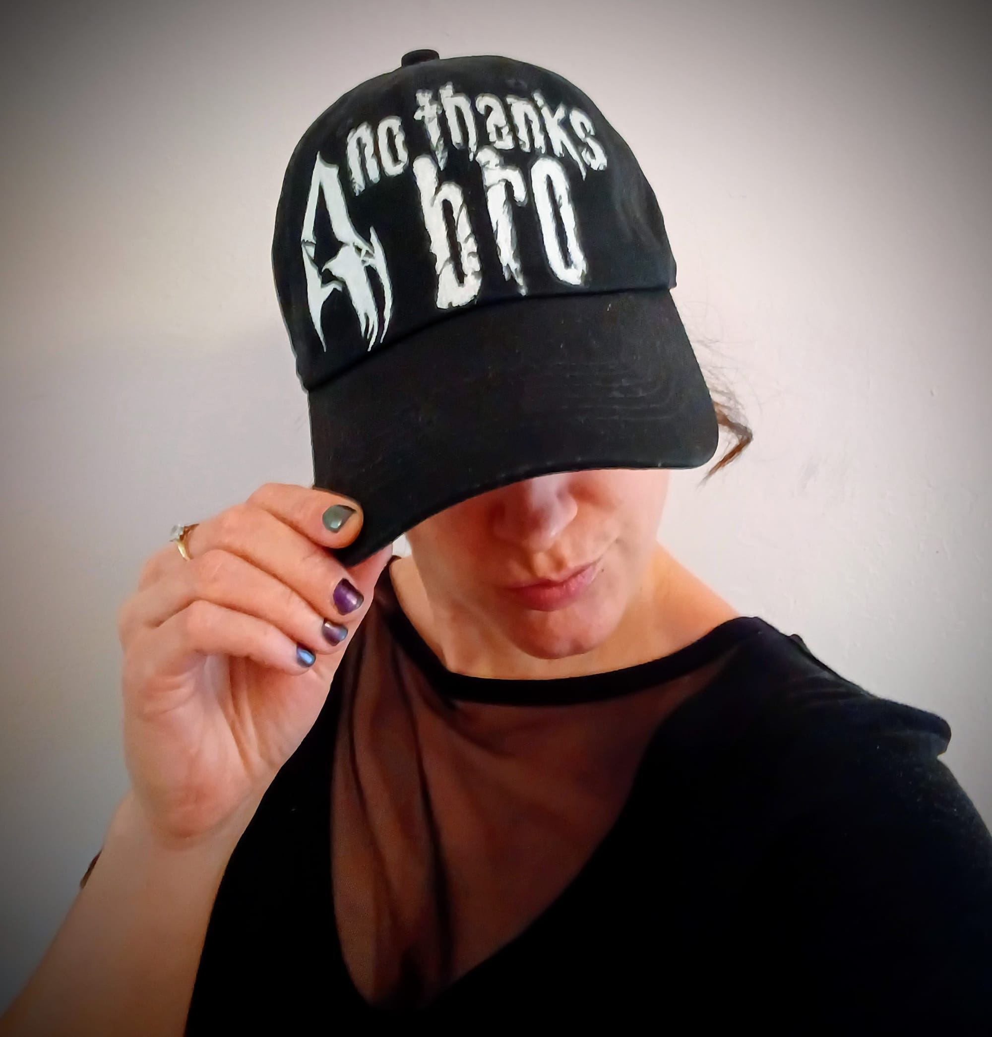 Selfie of me. I am looking down and tipping the cap of a black baseball cap so it covers my face and instead displays the front of the hat which reads "No thanks bro" in the Resident Evil 4 2005 style lettering. The RE4 logo is to the left of the words.